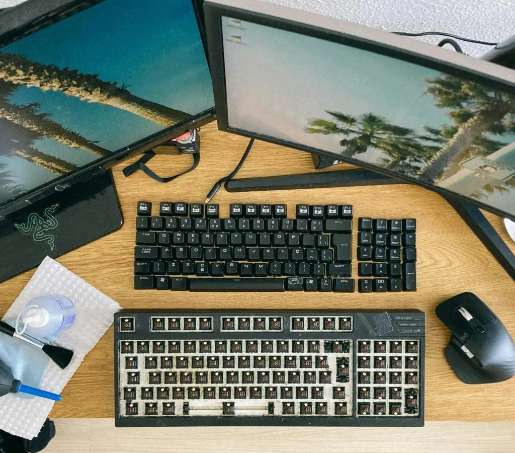 A person using a laptop and desktop dual setup, with monitors and keyboards side by side