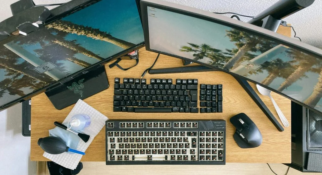 A person using a laptop and desktop dual setup, with monitors and keyboards side by side